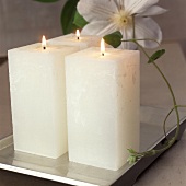Drei weiße hohe quadratische Kerzen auf einem blattversilb.Tablett