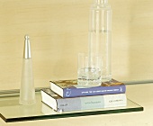 Detail; Glasregal mit Bücherstapel, Wasserglas und Parfumflasche