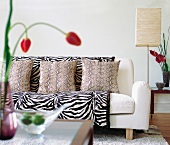White sofa with zebra fur blanket, snake pattern pillows and paper floor lamp