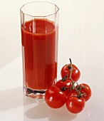 Ein Glas mit Tomatensaft,Freisteller neben dem Glas liegen Tomaten