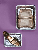 Abendtasche und Sandalette aus Metallic-Leder liegen in Aluschalen