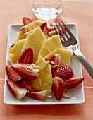 Fresh pineapple and strawberries with almond slivers on white plate