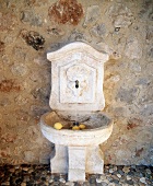 Schöner, alter Brunnen aus Stein vor einer Natursteinwand