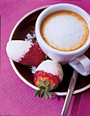 Schoko-Erdbeeren liegen neben einem Cappuccino