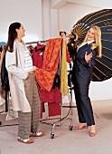 2 füllige Frauen bei der Auswahl von Klamotten vor Kleiderständer,lachen
