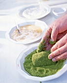 Close-up of man's hands breading piece of meat with mix of white bread and herbs