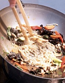 Close-up of bami goreng being prepared with mushrooms and noodles in a wok