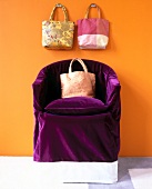 Purple velvet chair cover with three silk handbags against yellow background