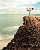 Young woman performing stretching exercise on cliff near sea