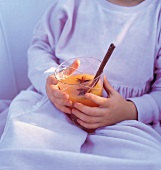 Kinderhände halten ein Glas mit Teepunsch im Schoß