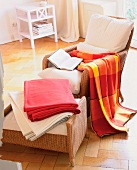Various wool plaid blankets on wicker armchair and footstool in living room