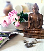 Buddha-Figur aus Holz vor einer Schale mit Pfingstrosen