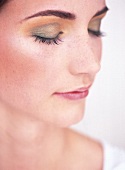 Close-up of pretty young woman wearing golden eye shadow, eyes closed in peace