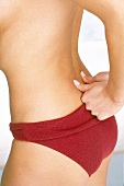 Close-up of woman wearing red knickers pushing both the thumbs on pelvic bone, mid section