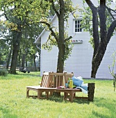 Gartenbank umrundet einen Baum vor einem weißen Holzhaus, Frühling
