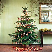 Christmas tree decorated with fruits, wooden figurines, baubles, pretzels and lit candles