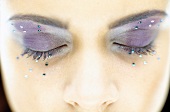 Close-up of woman's closed eyes wearing purple eye shadow decorated with rhinestones