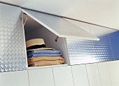 Folded textiles and hat in opened reflective foil cabinet with hinged doors