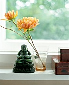Two dahlias in glass with green buddha figure on window sill