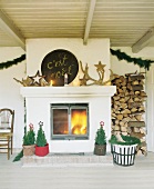 Fireplace with firewoods, antlers and Christmas tree in pots