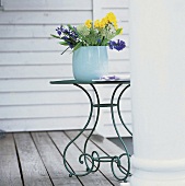 Frühlingsblumen in großer, blauer Glasvase auf romantischem Eisentisch