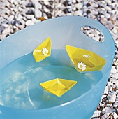 Gelbe Papierschiffchen schwimmen in türkisfarbenem Plastikzuber