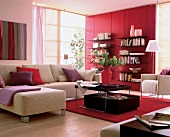 Helles Sofa mit Couchtisch auf rotem Teppich.Bücherrregal vor roter Wand