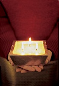 Frau hält viereckige, silberfarbene Kerze in der Hand