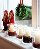 White pillar candles in jars covered with star anise and pink pepper on window sill