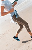 Frau läuft am Strand, grüne JoggingHose, blau-weißes Oberteil