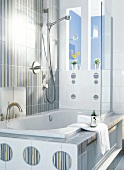 Striped tiles and bathtub with glass dividing wall in bathroom