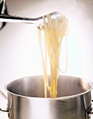 Close-up of tongs holding cooked spaghetti over vessel