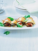 Four eggplant rolls with mint leaves served on dish