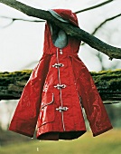 Kinderregenjacke in rot, gummiert, hängt am Baum, Still