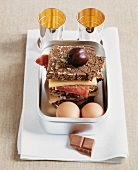 Two eggs and various snacks in steel box for a picnic