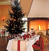 Festively decorated room with Christmas tree and table in front of burning fireplace
