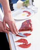 Close-up of preparation of beef carpaccio with knife on chopping board