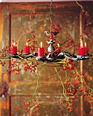 Lit red candles and branches of rosehips on chandelier