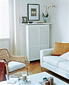 Radiator cover, white sofa and wicker chair in living room
