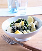 Rice with spinach, feta cheese and lemon wedges in a white bowl