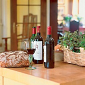 Bauernbrot, Rotweinflaschen, Glas Rotwein auf Holztisch