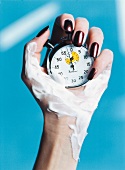 Close-up of woman's hand with nail varnish on nails and cream on hand, holding stop watch