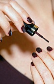 Frau lackiert ihre Fingernägel dunkel-violett
