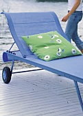 Green floral pattern cushion on blue sun lounger with wheels on wooden pier