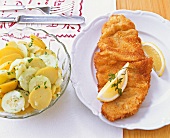 Wiener Schnitzel with lemon wedges on plate and bowl of potato salad
