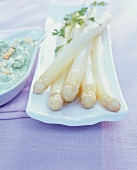 Close-up of white asparagus with herb sauce in serving dish