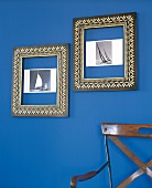 Zwei Schwarze Bilderahmen mit Gold - verzierung hängen an blauer Wand
