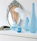 Hellblaue Glasvasen und Spiegel auf einer weiße Kommode