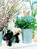Ornamental cherry, lilac and forget-me-not in metal vase and black stuffed toy