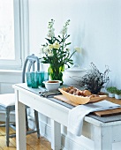 Basket of bread on wooden board, terrine, cutlery and vase of flowers on table